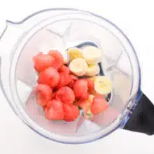 Fresh fruit is in a blender with protein powder and other smoothie ingredients.