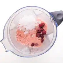 Looking down on a blender jar with pink liquid, raspberries, and crushed ice.