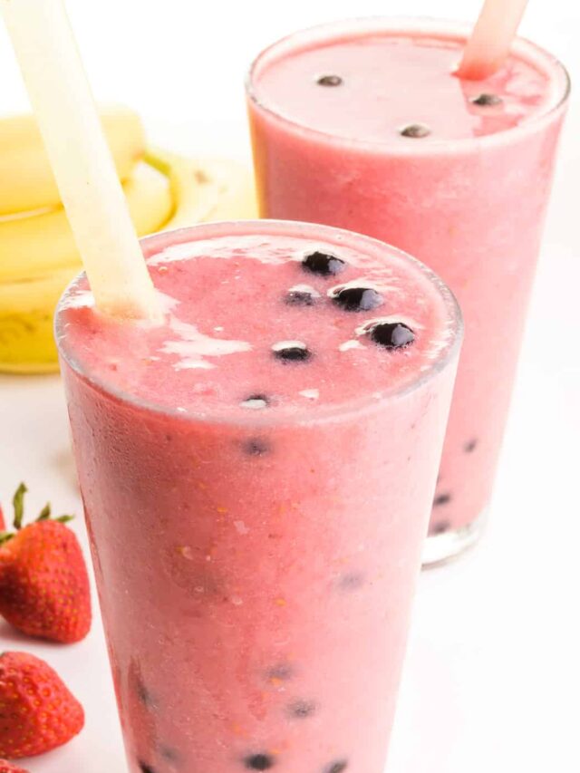 A boba smoothie is in a glass with another one behind it and fresh fruit around it.