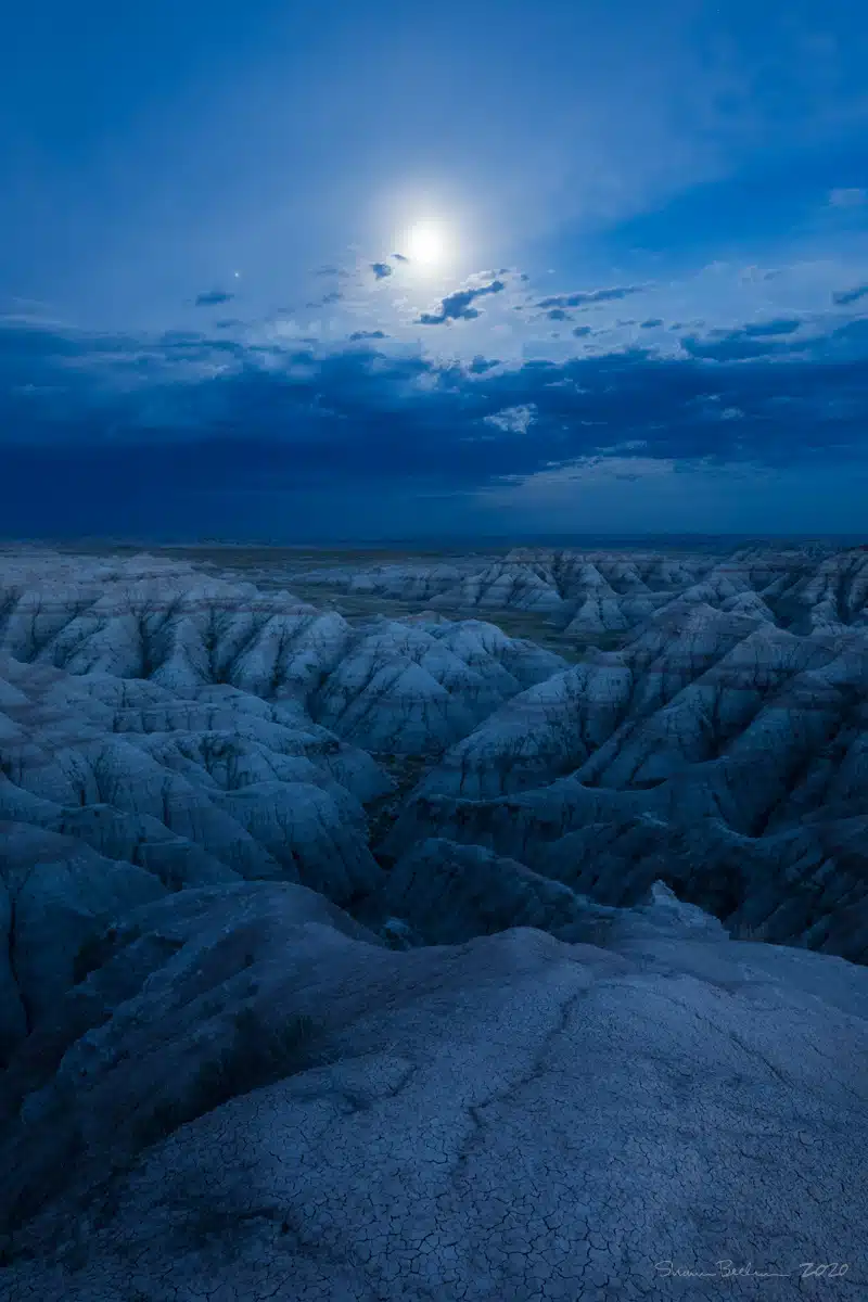 The moon shines bright over the South Dakota Badlands in this blue-hour landscape shot.