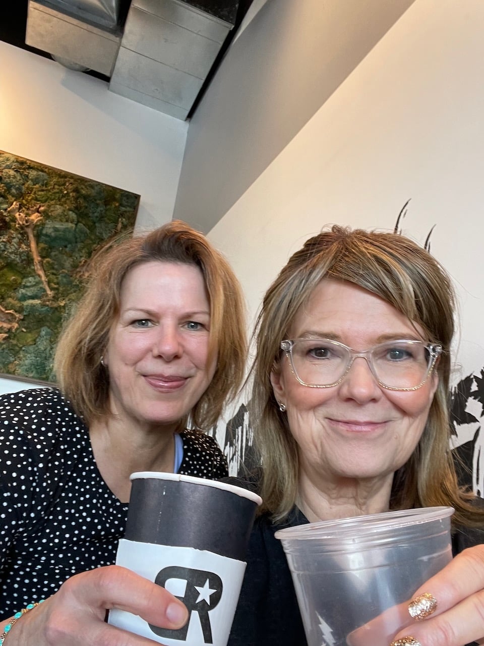 Marly and her cousin Melanie pose with their coffee and tea cups at a coffee shop.