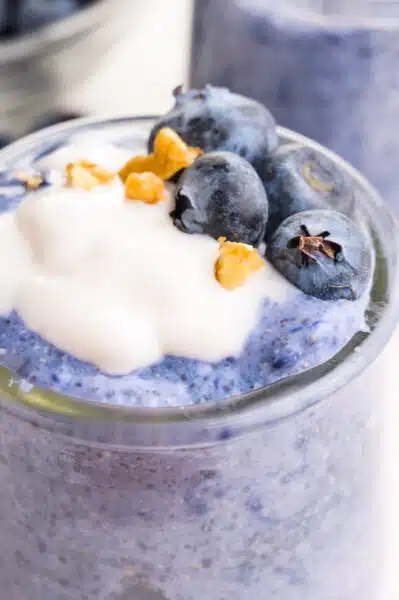 A closeup of blue chia pudding with dairy-free yogurt on top, chopped walnuts, and fresh blueberries.