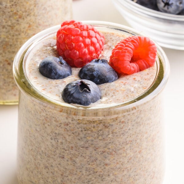 A closeup of chia flax pudding in a glass dish. It has fresh raspberries and blueberries on top.