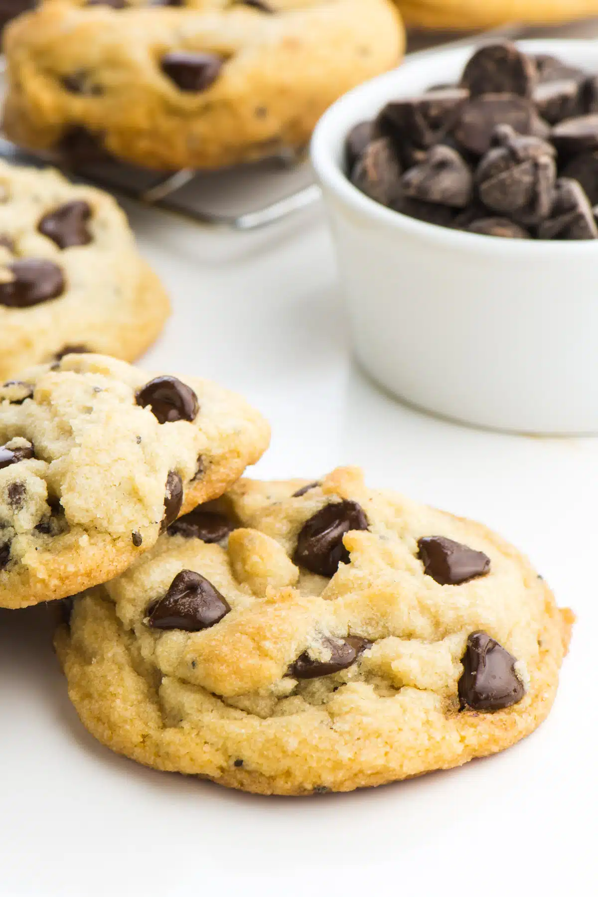 Several chocolate chip cookies are arranged near a bowl of vegan chocolate chips. 