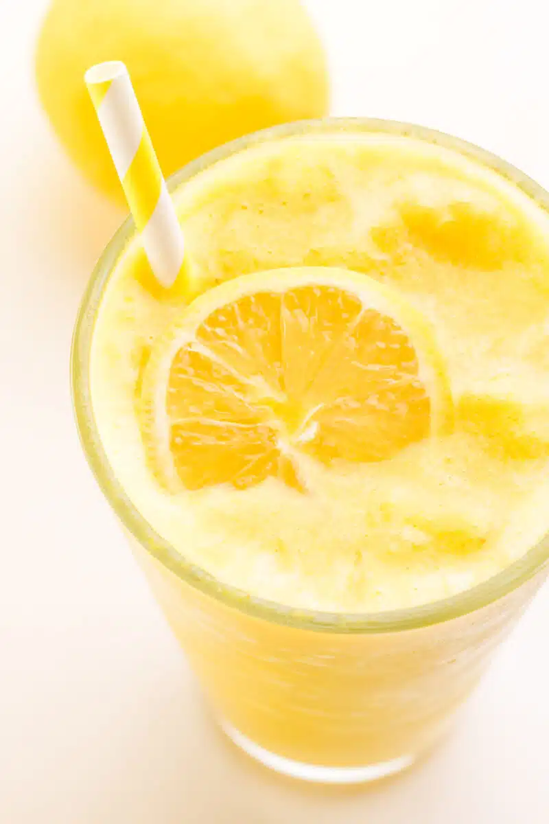 Looking down on a lemon smoothie with a lemon slice resting on top. There is a yellow straw and a fresh lemon in the background.