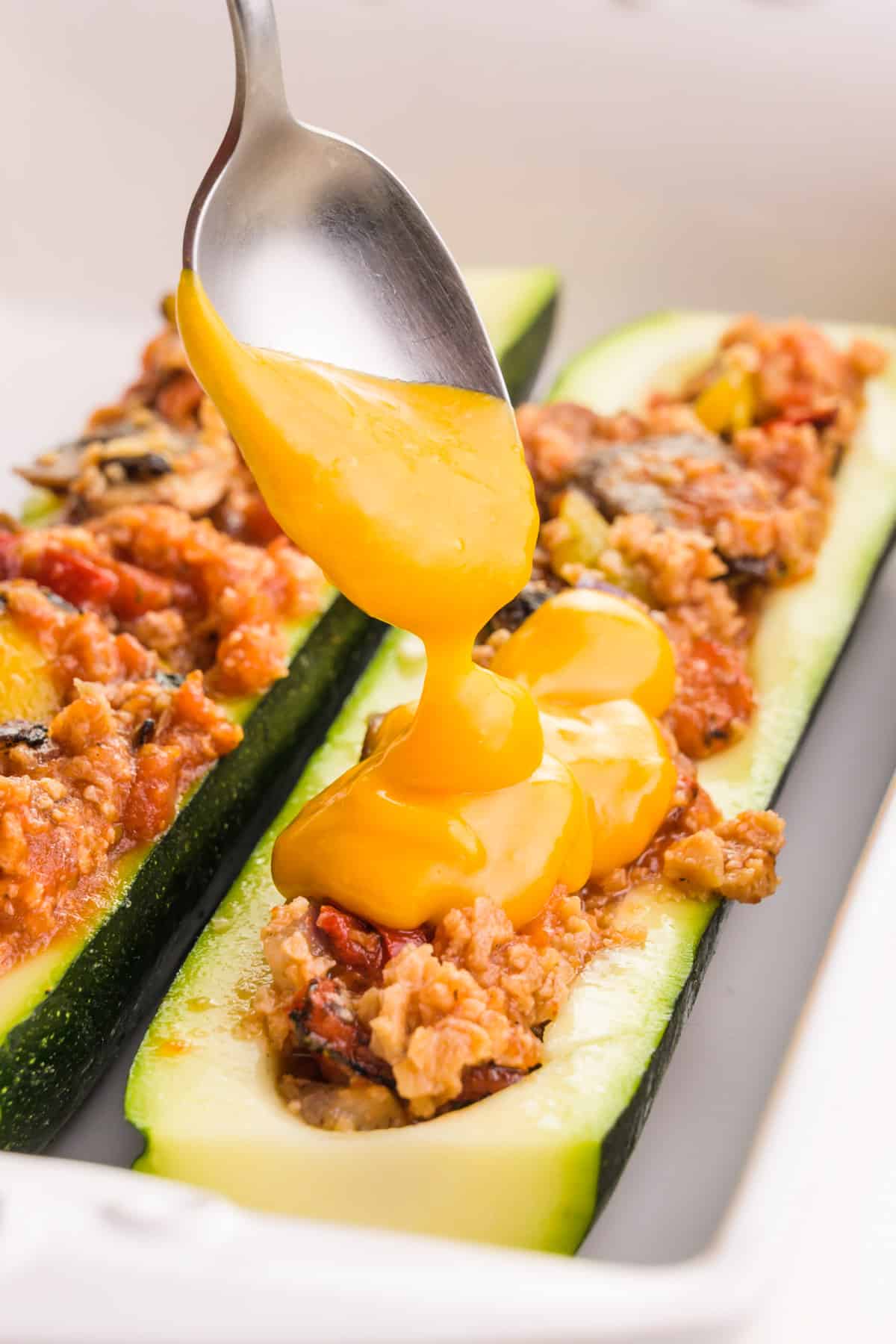 A spoonful of melted vegan cheese is drizzled over the zucchini boat.