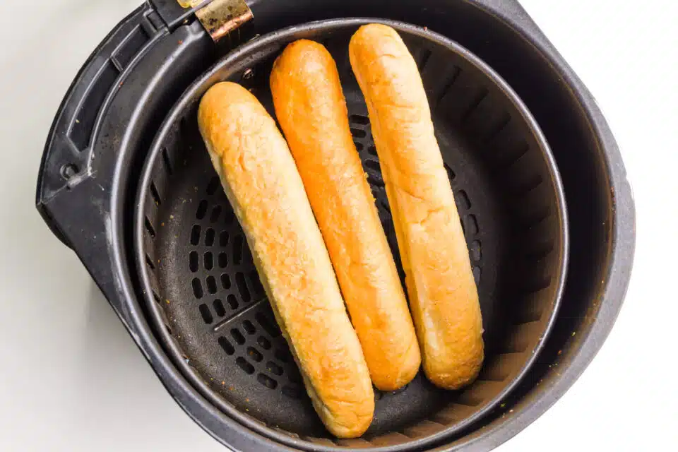 Three breadsticks are in an air fryer basket ready to be reheated. 
