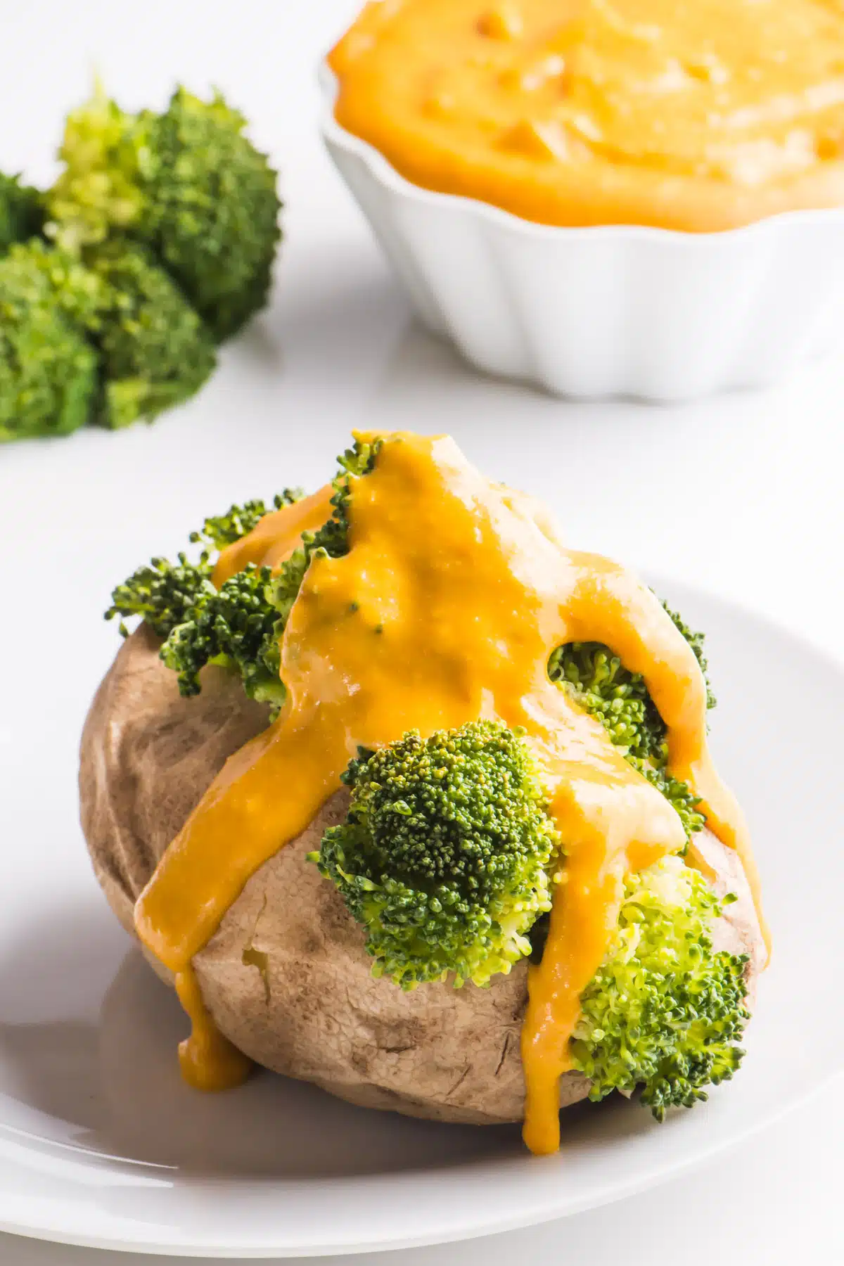 A baked potato is topped with steamed broccoli and vegan cheese sauce.