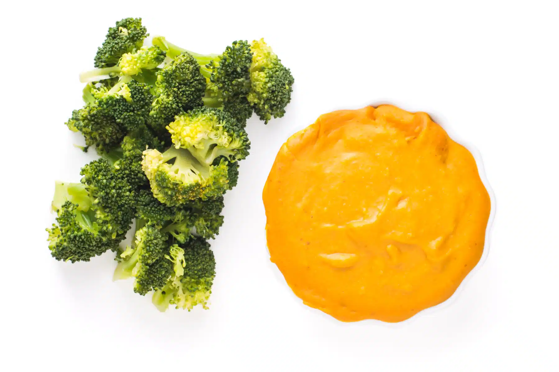 Looking down at a bright orange bowl of vegan cheese sauce next to steamed broccoli.