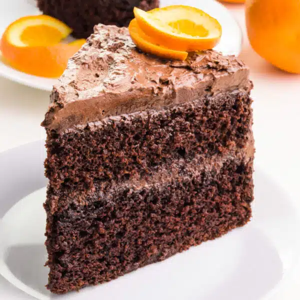 A slice of eggless orange chocolate cake sits on a plate.  There is an orange slice on top of the cake.