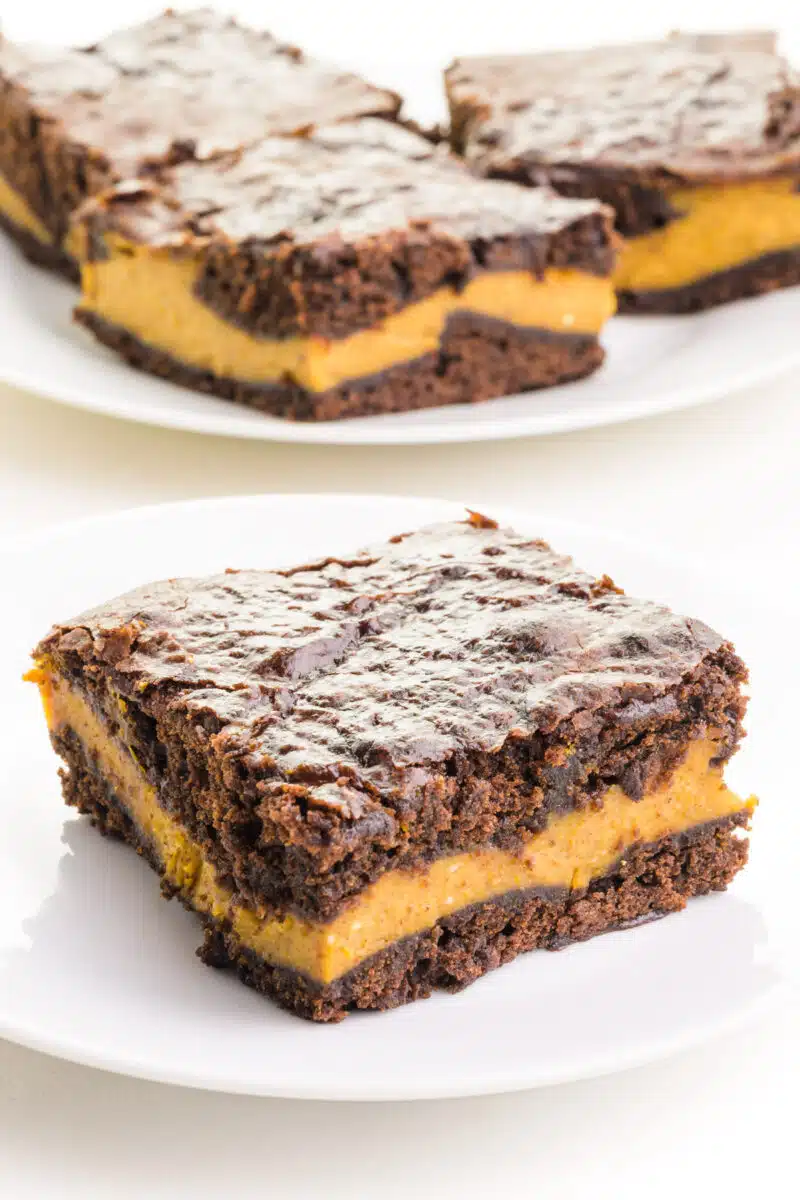 A vegan chocolate pumpkin brownie sits on a plate in front of more brownies in the background.