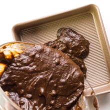 Chocolate brownie batter is being poured into a baking pan.