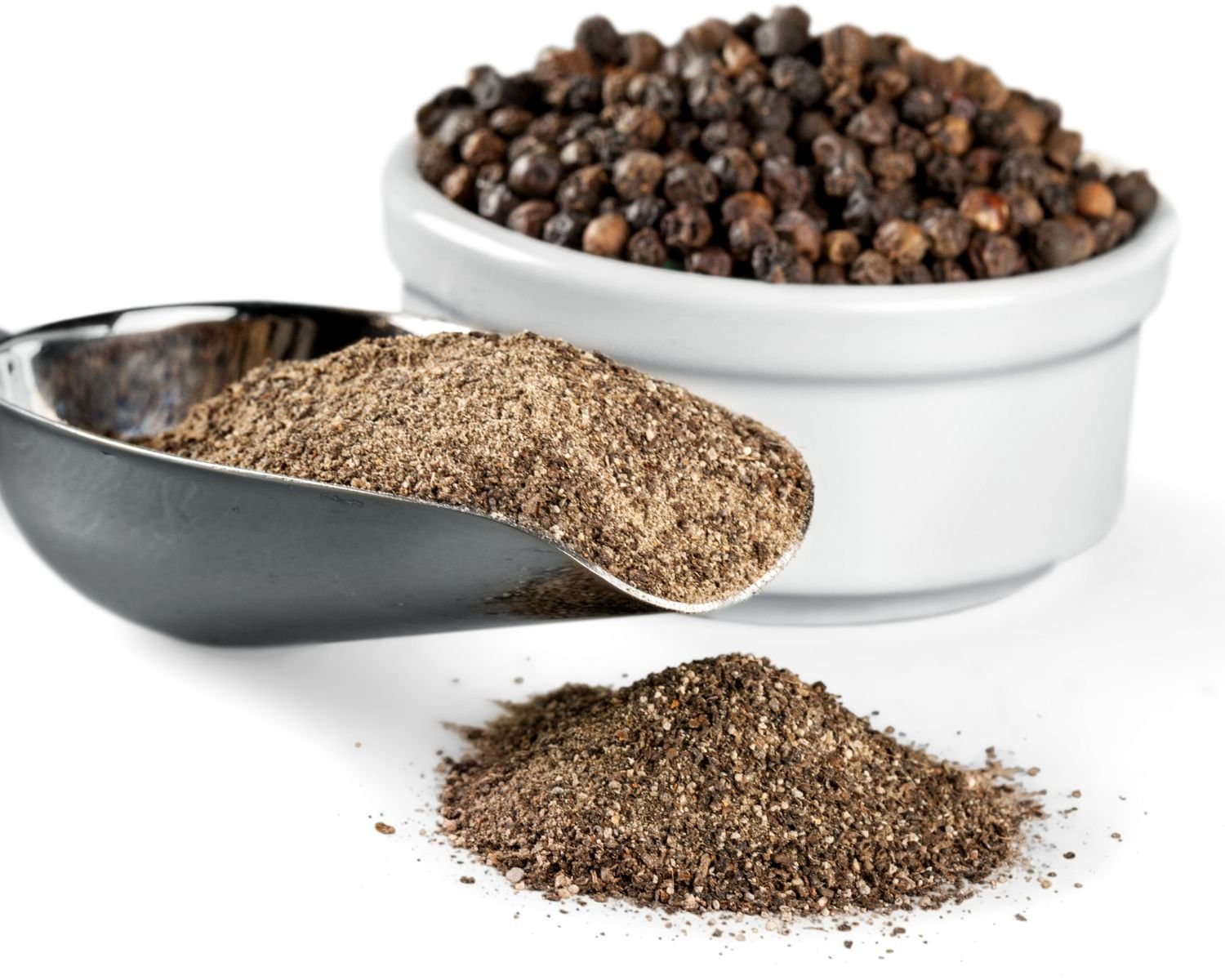 Peppercorns are in a bowl and a large scoop has freshly ground black pepper and some of it is scattered in front of the scoop.