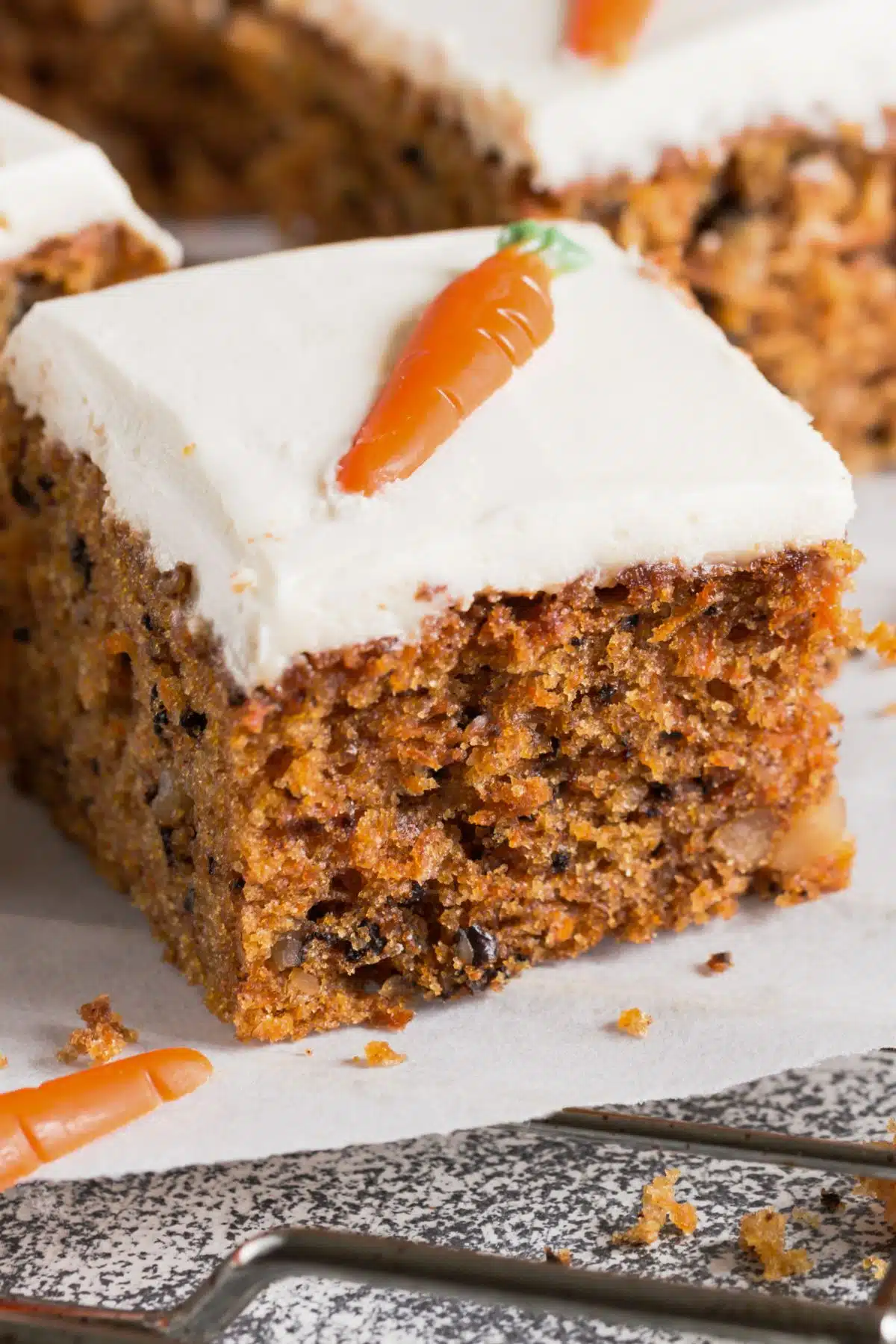 A slice of cake has white frosting and a frosting carrot on top. 