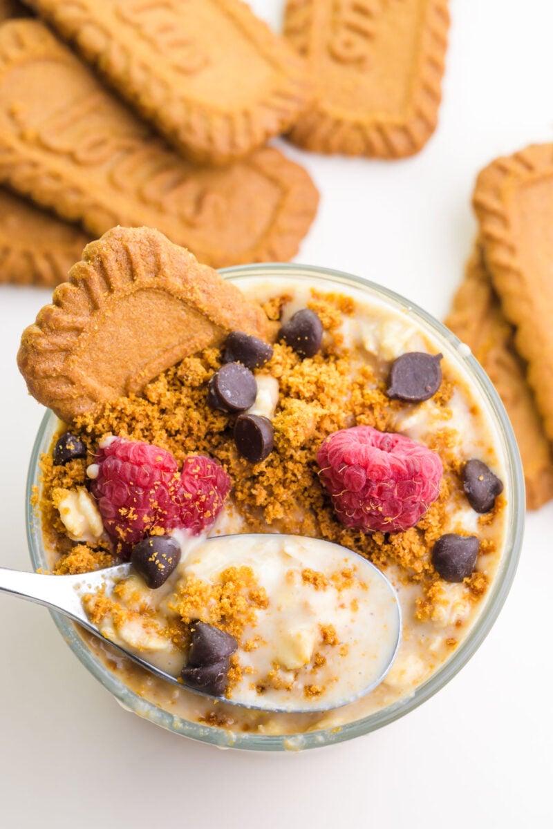 Looking down on a jar of biscoff cookie overnight oats with a spoon in it. There are cookie beside the jar.