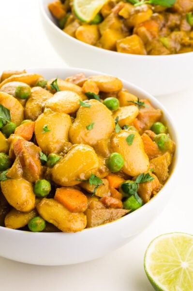 A bowl of butter bean curry sits in front of another bowl in the background. There is a fresh lemon beside the front bowl.