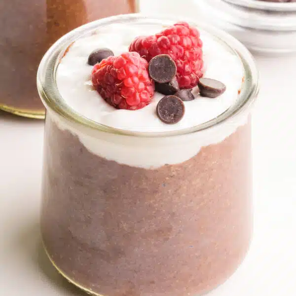 A jar of flax pudding has yogurt, fresh raspberries, and chocolate chips on top.