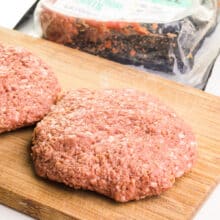 Hand-pressed burger patties are on a wooden cutting board, sitting in front of an opened package of Impossible Burger grounds.