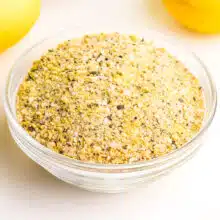 A closeup of lemon pepper seasoning in a bowl. Fresh lemons are barely visible in the background.