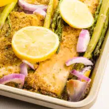 Lemon pepper tofu is in a pan with lemon wedges, red onions, and asparagus.