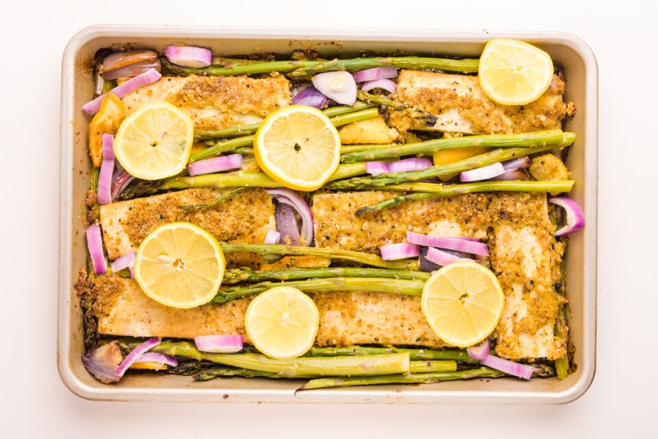 Looking down on a pan with freshly baked lemon tofu, asparagus, and lemon wedges.