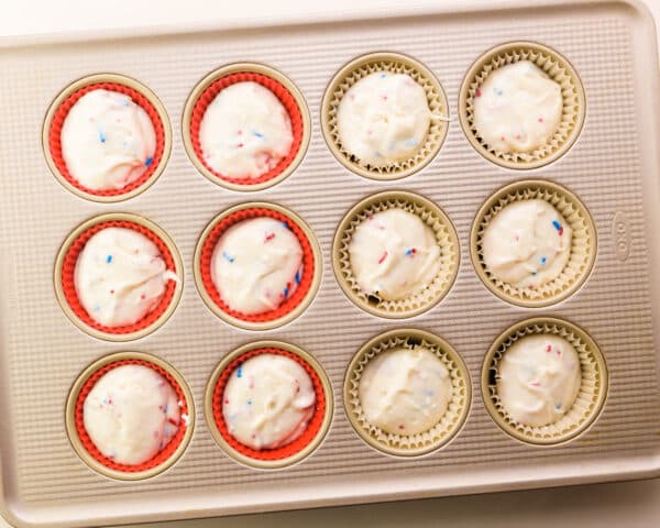 Looking down on a muffin pan with paper and silicone liners filled with cupcake batter.
