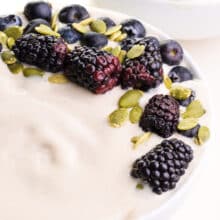 A closeup of vanilla smoothie bowl shows blackberries and blueberries on top along with pumpkin seeds.