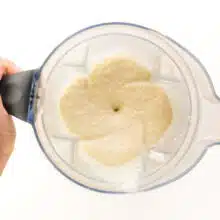 A hand holds a blender jar with freshly blended vanilla protein smoothie inside.