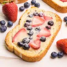 A slice of dairy-free custard toast has berries on top. It sits beside fresh blueberries and strawberries.