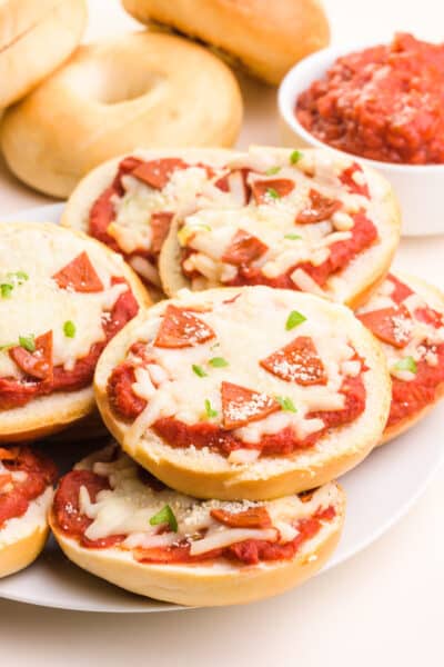 A stack of vegan mini bagel bites sits in front of a bowl of marinara sauce and more mini bagels in the background.