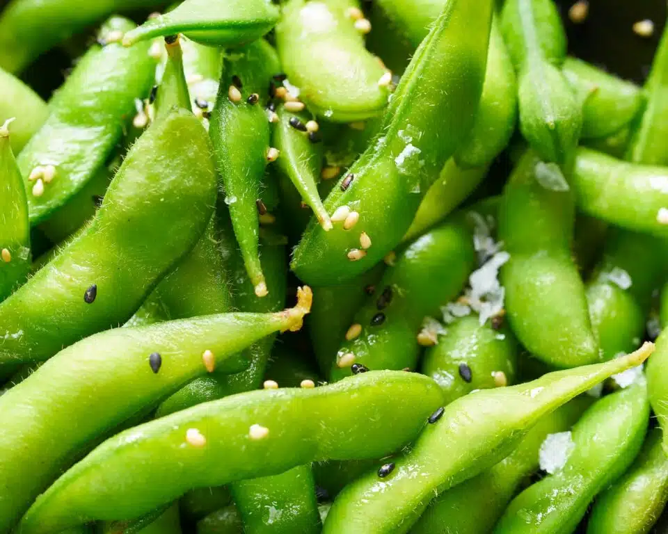 Looking down on edamame pods topped with sesame seeds and garlic bits.