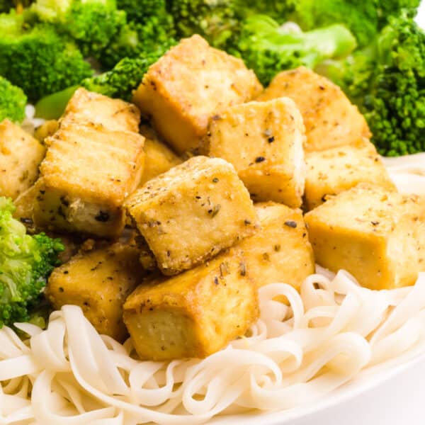 Cooked tofu is served with noodles and roasted broccoli.