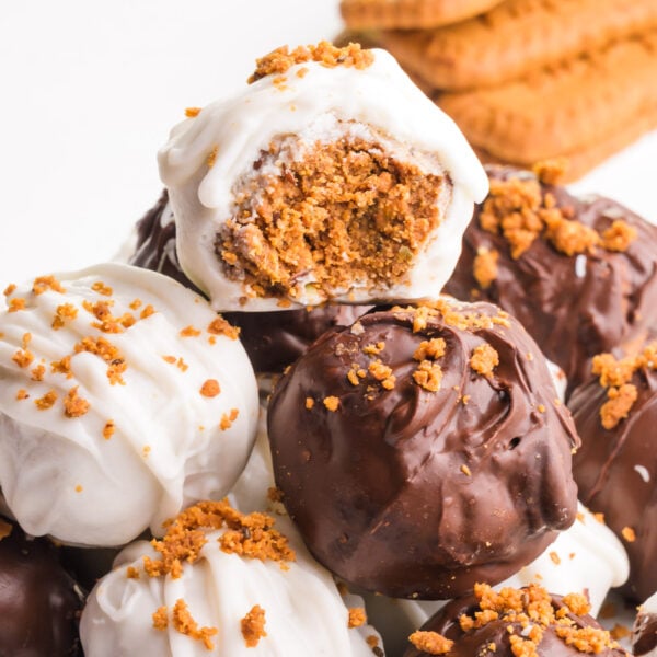 A stack of biscoff truffles shows the top one with a bite taken out. Biscoff cookies are barely visible in the background.