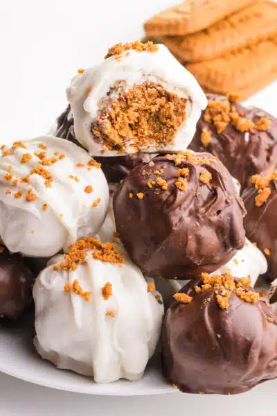 A stack of biscoff truffles shows the top one with a bite taken out. There are biscoff cookies in the background.