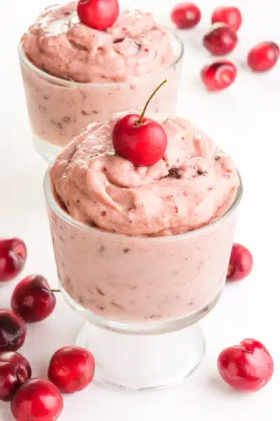 Two bowls of cherry nice cream have fresh cherries on top and around them.