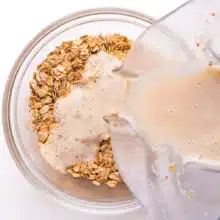 A milk mixture is being poured from a blender into a bowl with oats.