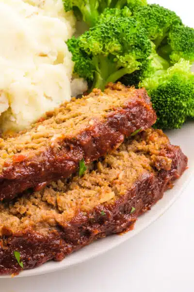 Two slices of Impossible meat meatloaf sit in front of mashed potatoes and broccoli on a plate.