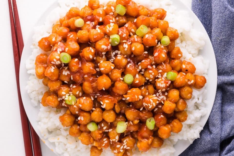 Looking down on a bowl of sticky chickpeas served over rice. There's a blue dish towel on the right and chopsticks on the left.