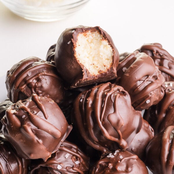 A stack of coconut balls sit on a plate. The top one shows a bite taken out.