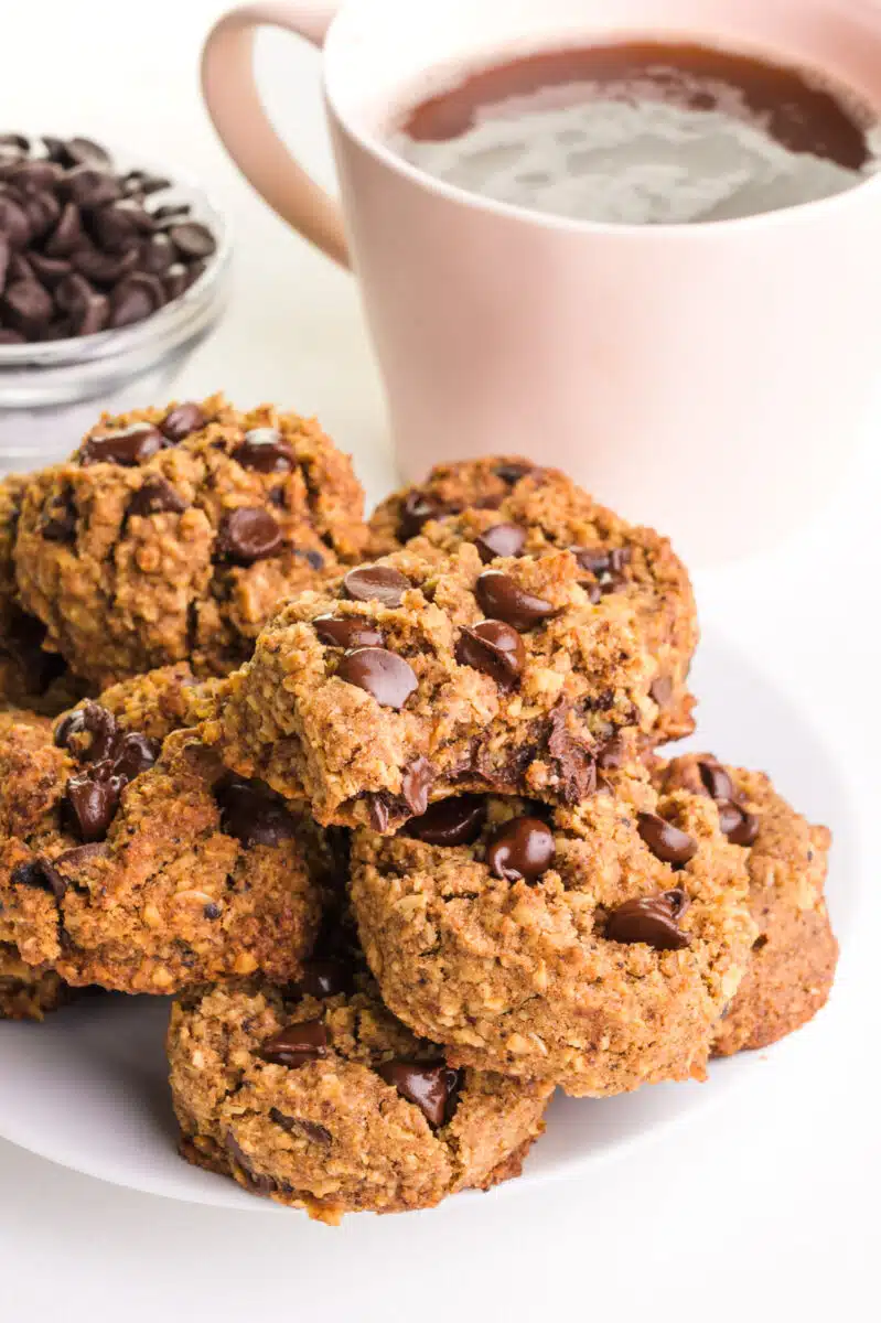 A plate of chocolate chip cookies sits in front of a bowl of chocolate chips and a cup of coffee.