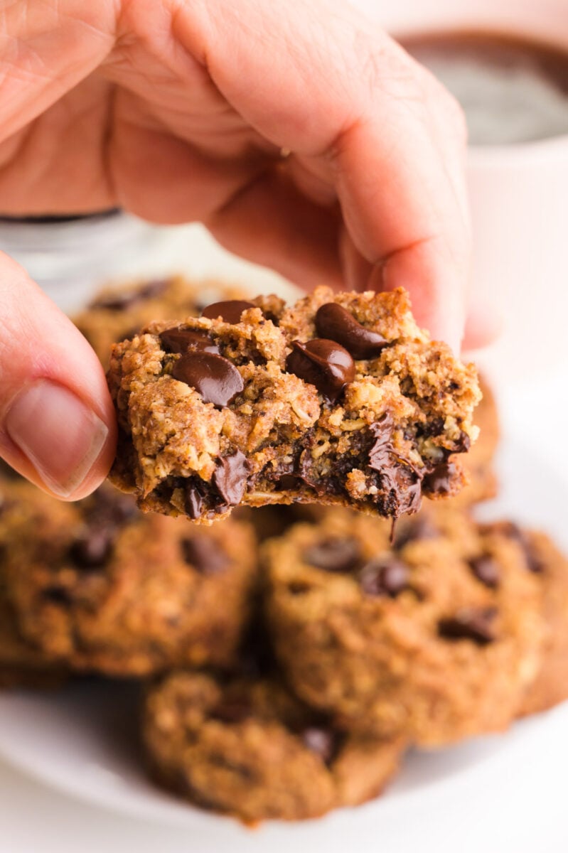 A hand holds a chocolate chip cookies with a bite taken out of it.