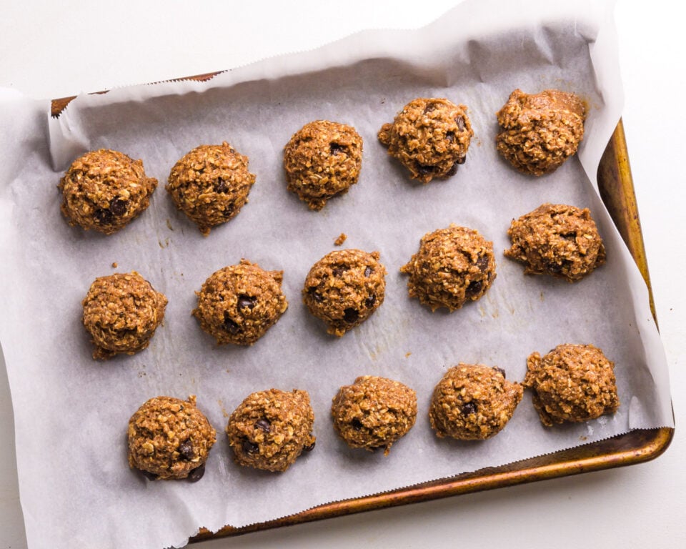 Cookie dough balls are side-by-side on a baking sheet lined with parchment paper.