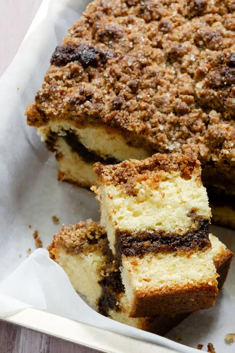 A slice of coffee cake is in the baking dish with the rest of the cake. It sits on its side, showing layers of cake with cinnamon filling in the middle.