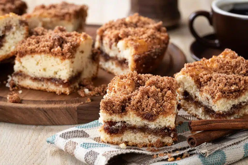Several slices of coffee cake sit on a table with napkins and cups of coffee.
