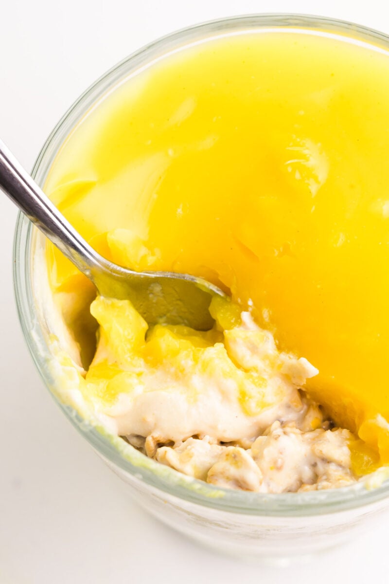 Looking down on a bowl of overnight oats topped with lemon curd. Threre is a spoon in the bowl, showing the oats inside.