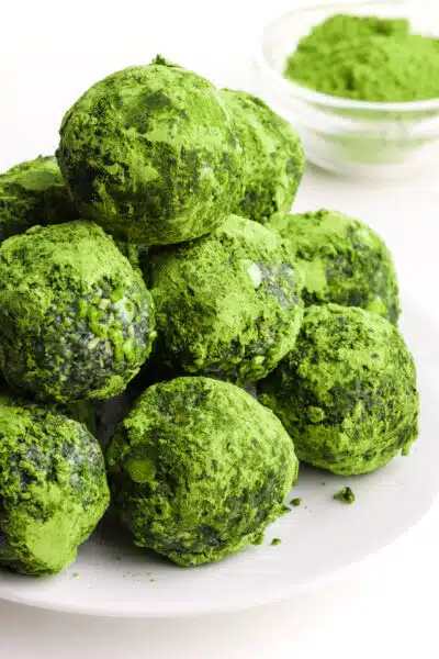 A stack of spirulina energy balls sits on a plate in front of a bowl of matcha tea powder.