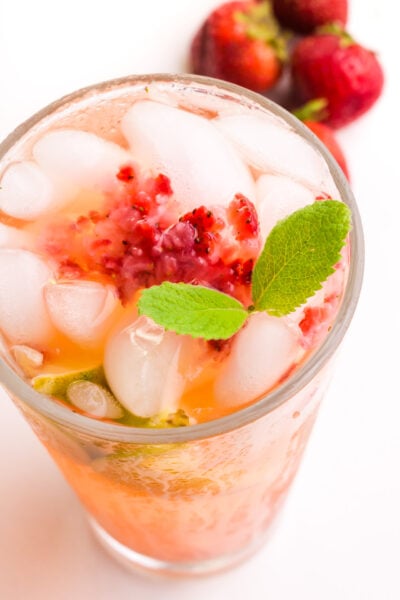 Looking down on a glass of green tea with strawberries and mint. There are fresh strawberries in the background.
