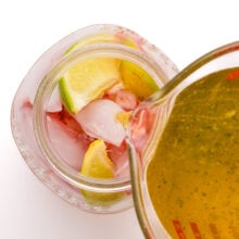 Green tea is being poured from a pyrex measuring cup into a mason jar with ice, mashed strawberries, and, lime slices.