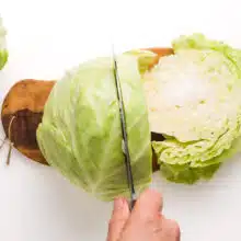 A hand uses a knife to cut cabbage in slices on a cutting board.