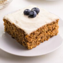 A slice of cake on a plate. There is white frosting and blueberries on top of the cake.